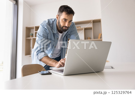Concentrated young man leaning over work desk type on notebook Concentrated young man leaning over work desk type on notebook 125329764