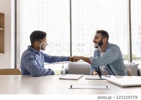 Smiling motivated young male teammates exchange fist bump at workplace 125329778