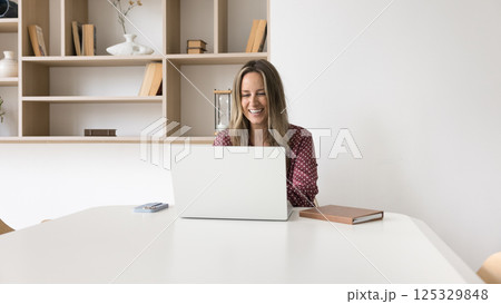 Smiling mature businesswoman sitting at table communicating online using notebook Smiling mature businesswoman sitting at table communicating online using notebook 125329848