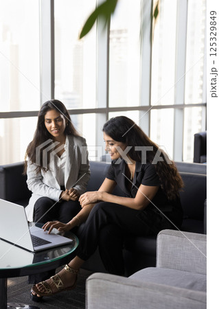 Two multinational women met in office lounge area with laptop Two multinational women met in office lounge area with laptop 125329849