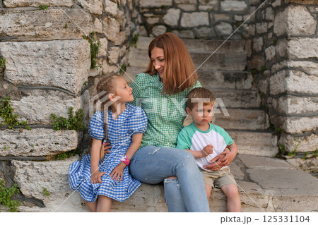 Mother hugs son and daughter near stone wall 125331104