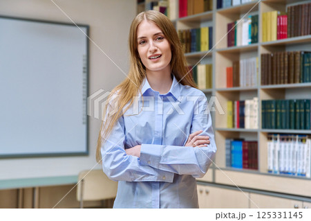 Portrait of teenage college student girl with crossed arms, inside library Portrait of teenage college student girl with crossed arms, inside library 125331145