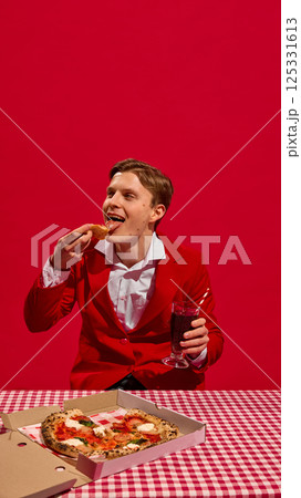 Man in red suit expressing satisfaction, enjoying pizza and soda at red checkered table against bold red background. Man in red suit expressing satisfaction, enjoying pizza and soda at red checkered table against bold red background. 125331613