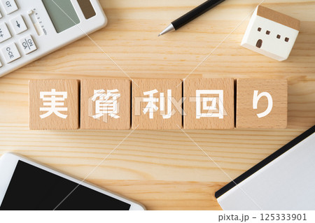 実質利回りと書かれたブロック、電卓、スマホ、建物の模型 実質利回りと書かれたブロック、電卓、スマホ、建物の模型 125333901