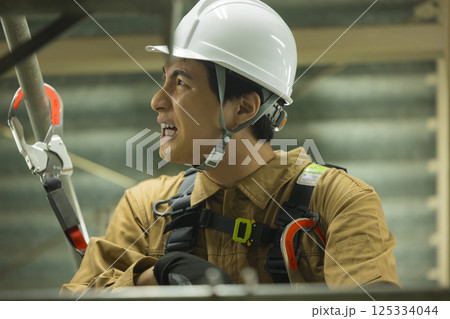 フルハーネスを装着し足場を登る作業員の男性　 125334044