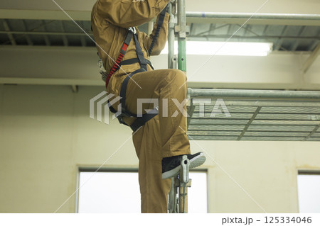 フルハーネスを装着し足場を登る作業員の男性　 125334046