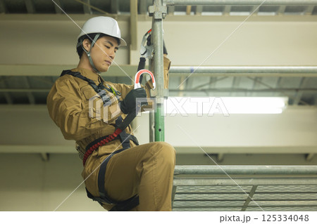 フルハーネスを装着し足場を登る作業員の男性　 125334048