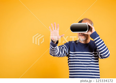 Portrait Asian smiling old man touching at something in a virtual reality glasses headset studio shot isolated yellow background, Excited happy senior man pensioner using VR play simulation game 125334172