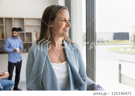 Successful mid aged businesswoman standing by window with confident smile Successful mid aged businesswoman standing by window with confident smile 125336471