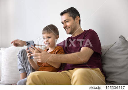 Happy father tween son relax on sofa interact with smartphone Happy father tween son relax on sofa interact with smartphone 125336517