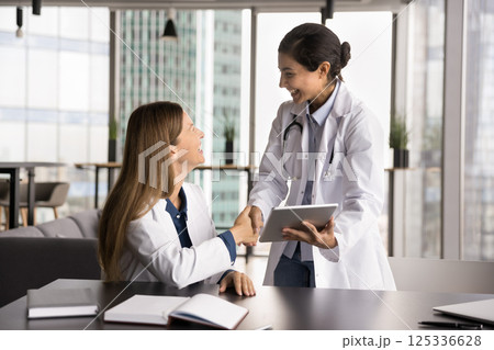 Young female medic intern shake hand of smiling woman mentor 125336628