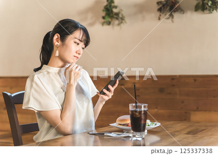 ランチを食べに来たカフェや飲食店の口コミ・SNSをスマホで見るアジア人女性 ランチを食べに来たカフェや飲食店の口コミ・SNSをスマホで見るアジア人女性 125337338