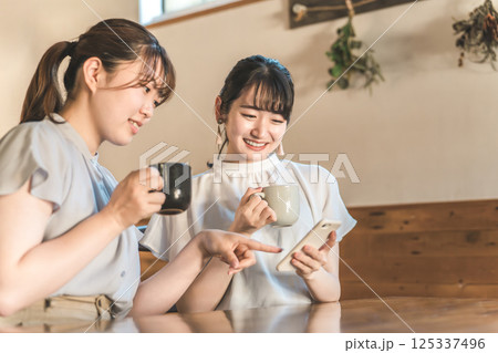 カフェでスマホを見ながら話す笑顔のアジア人女性 カフェでスマホを見ながら話す笑顔のアジア人女性 125337496