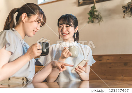 カフェでスマホを見ながら話す笑顔のアジア人女性 125337497