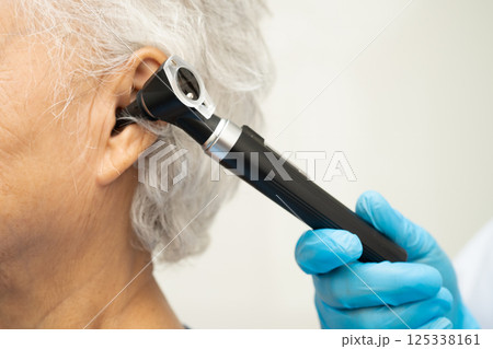 Otolaryngologist or ENT physician doctor examining senior patient ear with otoscope, hearing loss problem. 125338161