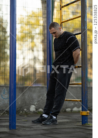 man dressed in black athletic clothing performs workout outdoor gym in city park. setting has serene atmosphere trees in background during daylight. man dressed in black athletic clothing performs workout outdoor gym in city park. setting has serene atmosphere trees in background during daylight. 125338825