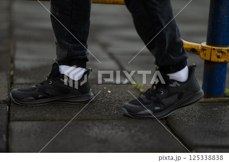 person wearing black athletic shoes and ankle length pants is exercising on textured pavement. cloudy sky adds energetic atmosphere of workout session. 125338838