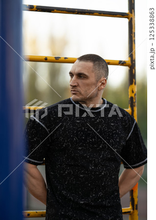 male athlete stands confidently set of exercise bars dressed in fitness attire. golden hour light casts warm glow highlighting his focused expression and strong physique. male athlete stands confidently set of exercise bars dressed in fitness attire. golden hour light casts warm glow highlighting his focused expression and strong physique. 125338863