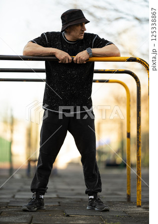 man is actively using outdoor fitness equipment wearing casual athletic clothing. He stands confidently and focuses on his workout routine in city park during early morning light. man is actively using outdoor fitness equipment wearing casual athletic clothing. He stands confidently and focuses on his workout routine in city park during early morning light. 125338867