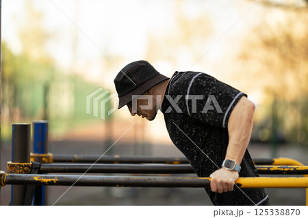 Focused individual engages in fitness training performing dips on parallel bars outdoor gym. scene captures sunny day clear background enhancing workout atmosphere. 125338870