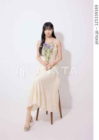 Cropped view of young woman sitting in white dress holding bouquet of purple flowers 125339169