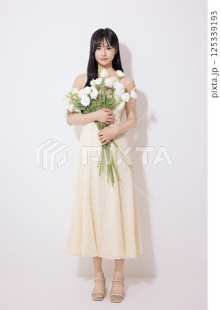 Portrait of a young woman standing wearing a white dress and holding a bouquet of white flowers 125339193