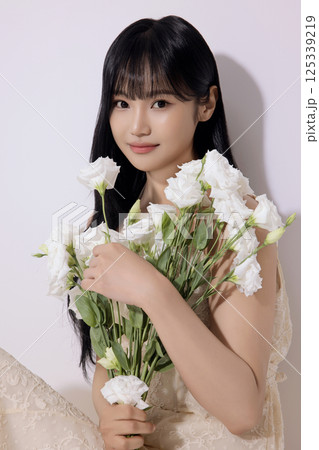 Portrait of a young woman sitting wearing a white dress and holding a bouquet of white flowers 125339219