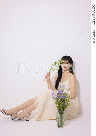 A young woman in her 20s sitting in front of a vase 125339220