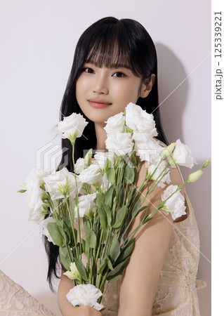 Portrait of a young woman sitting wearing a white dress and holding a bouquet of white flowers 125339221