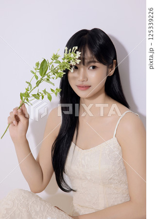 Portrait of a young woman sitting and holding flowers Portrait of a young woman sitting and holding flowers 125339226