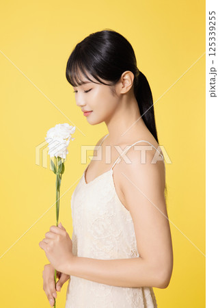 Portrait of young woman standing wearing white dress and holding white flowers 125339255