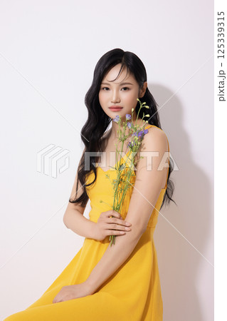 Portrait of young woman wearing yellow dress and holding bouquet of flowers 125339315