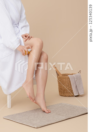 Wearing a shower gown and applying oil to legs 125340139