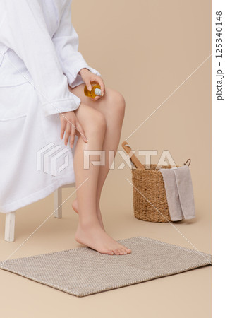 Wearing a shower gown and applying oil to legs 125340148