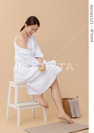 Cropped view of young woman wearing robe and applying oil to skin after shower Cropped view of young woman wearing robe and applying oil to skin after shower 125340166