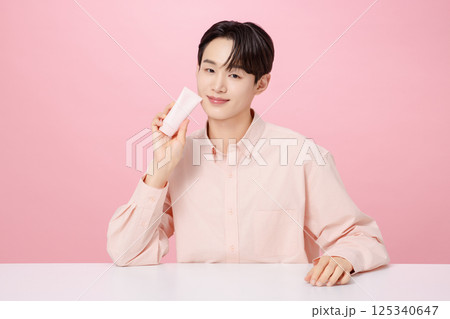 Portrait of a young man posing while holding a tube product Portrait of a young man posing while holding a tube product 125340647