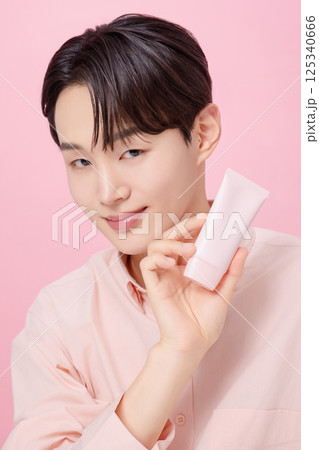 Portrait of a young man posing while holding a tube product Portrait of a young man posing while holding a tube product 125340666