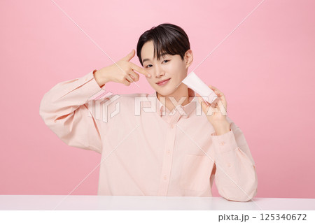 Portrait of a young man posing while holding a tube product Portrait of a young man posing while holding a tube product 125340672