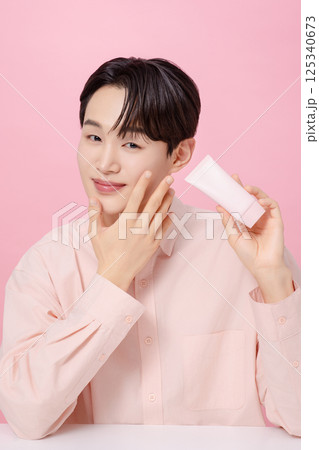 Portrait of a young man posing while holding a tube product Portrait of a young man posing while holding a tube product 125340673