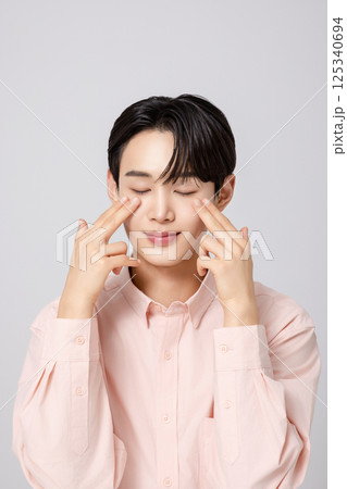 Portrait of a young man smiling while touching his face with his hands 125340694