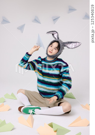 Cropped view of young man wearing bunny hat sitting surrounded by paper airplanes 125340819