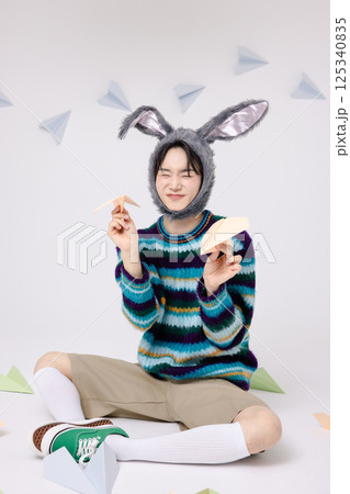 Cropped view of young man wearing bunny hat sitting surrounded by paper airplanes Cropped view of young man wearing bunny hat sitting surrounded by paper airplanes 125340835