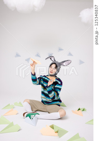 Cropped view of young man wearing bunny hat sitting surrounded by paper airplanes Cropped view of young man wearing bunny hat sitting surrounded by paper airplanes 125340837
