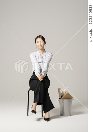 A neat-looking young woman in her 20s sitting on a chair next to a trash can containing drugs and syringes 125340932