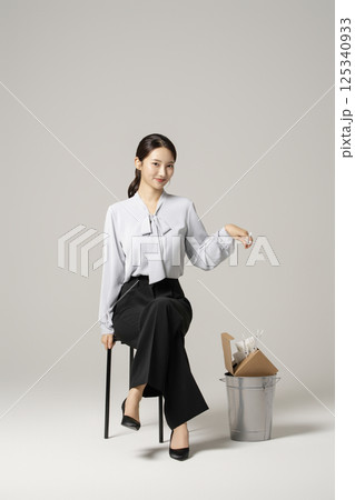 A neat-looking young woman in her 20s sitting on a chair next to a trash can containing drugs and syringes 125340933