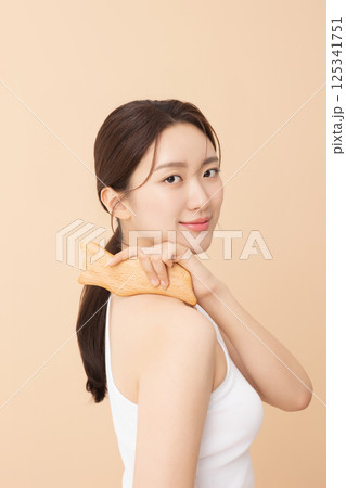 Portrait of a young woman massaging her shoulders with a gua sha 125341751