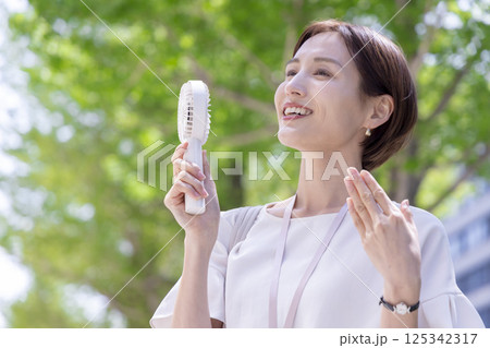 ビジネス ハンディファンで涼みながらオフィス街を歩く女性 ビジネス ハンディファンで涼みながらオフィス街を歩く女性 125342317