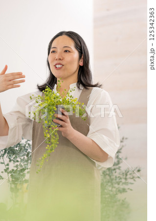 室内で植物の世話をする笑顔の大人女性|花屋園芸店教室イメージ|ウェルビー女子|ウェルビーイング 室内で植物の世話をする笑顔の大人女性|花屋園芸店教室イメージ|ウェルビー女子|ウェルビーイング 125342363