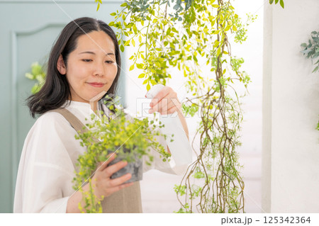 室内で植物の世話をする笑顔の大人女性｜花屋園芸店教室イメージ｜ウェルビー女子｜ウェルビーイング 125342364