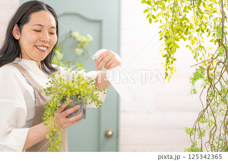 室内で植物の世話をする笑顔の大人女性|花屋園芸店教室イメージ|ウェルビー女子|ウェルビーイング 室内で植物の世話をする笑顔の大人女性|花屋園芸店教室イメージ|ウェルビー女子|ウェルビーイング 125342365